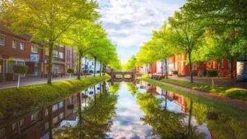A canal with mirrored reflections of trees and buildings, a bridge, and a clear sky.