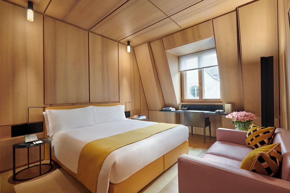 A modern hotel room with a large bed, a desk, and a sofa.