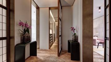A hallway with wooden flooring, two black console tables with potted orchids, and a view into a room with a pink sofa and a table.