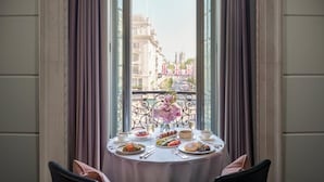 A dining table set with various dishes and a vase of flowers, positioned by a window with a view of buildings. - Hotel Cafe Royal, London (London)