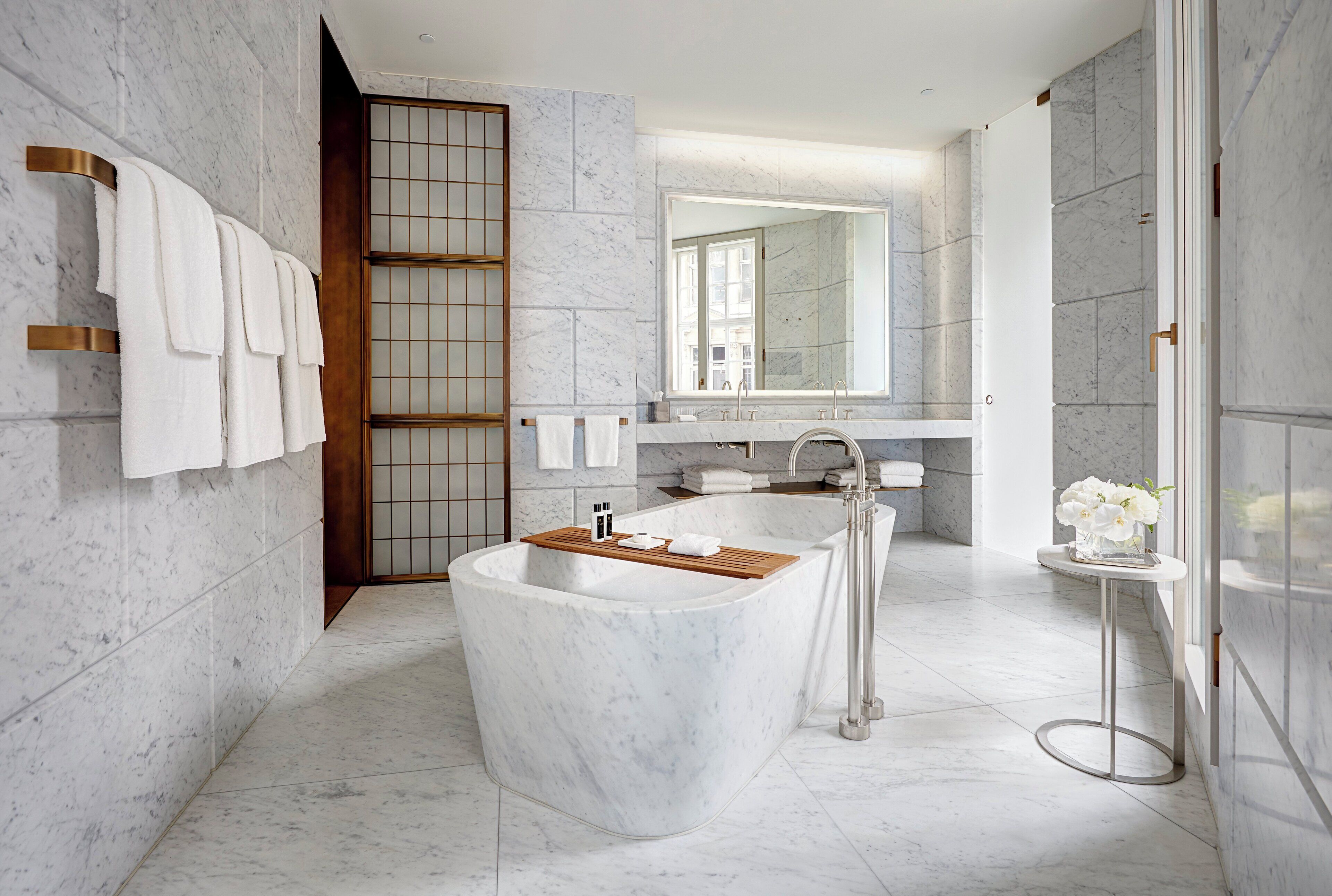 Un baño moderno con una bañera independiente, un espejo grande y paredes de mármol.
