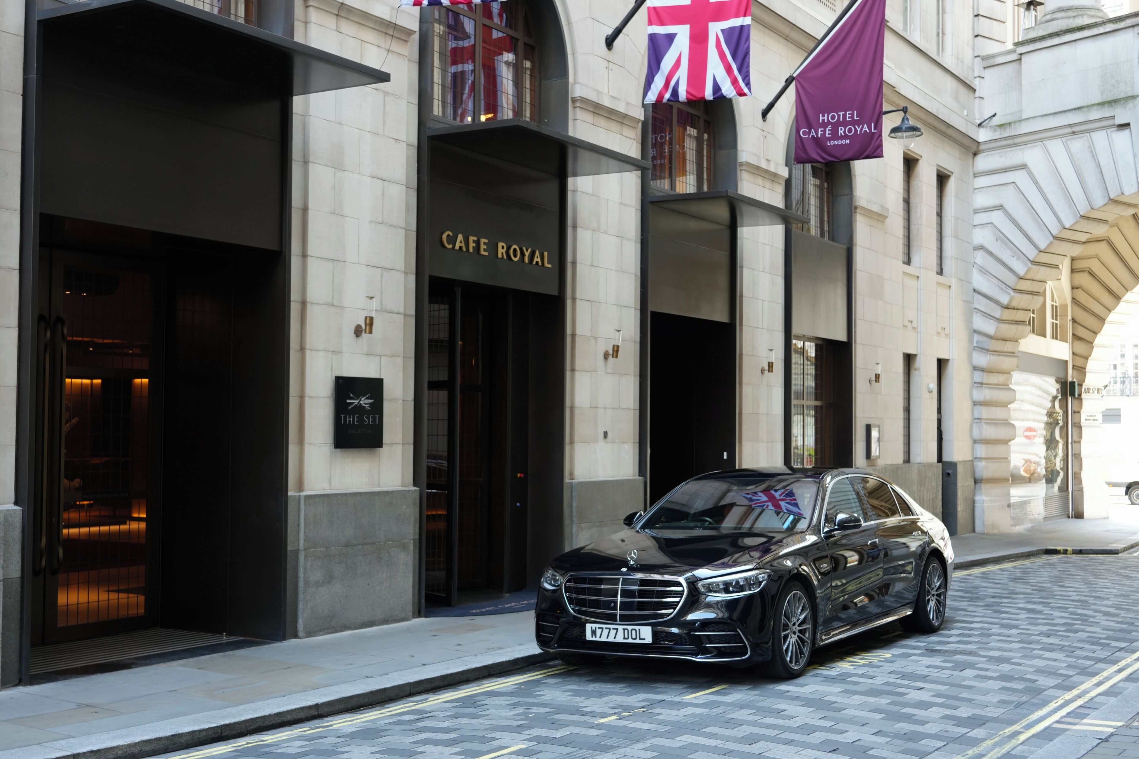 A black car parked in front of a building with 'Café Royal' signage.
