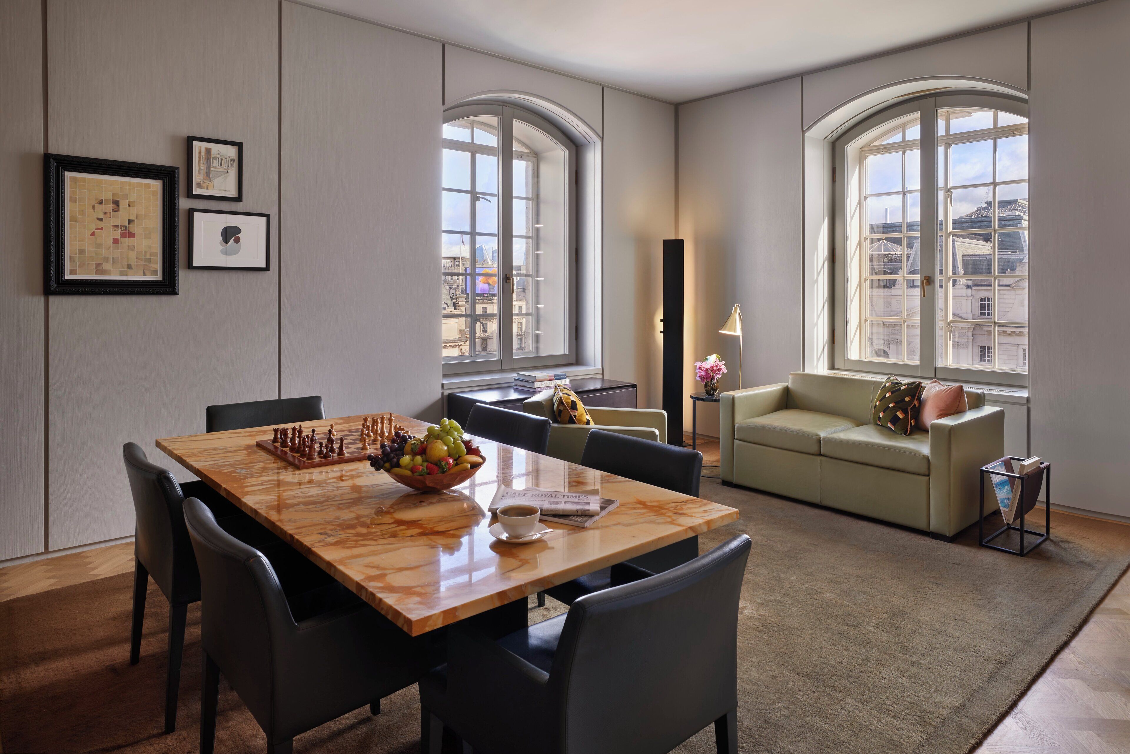 Un comedor moderno con una mesa de madera, sillas y un bol de fruta. Se ve un sofá y una lámpara al fondo.