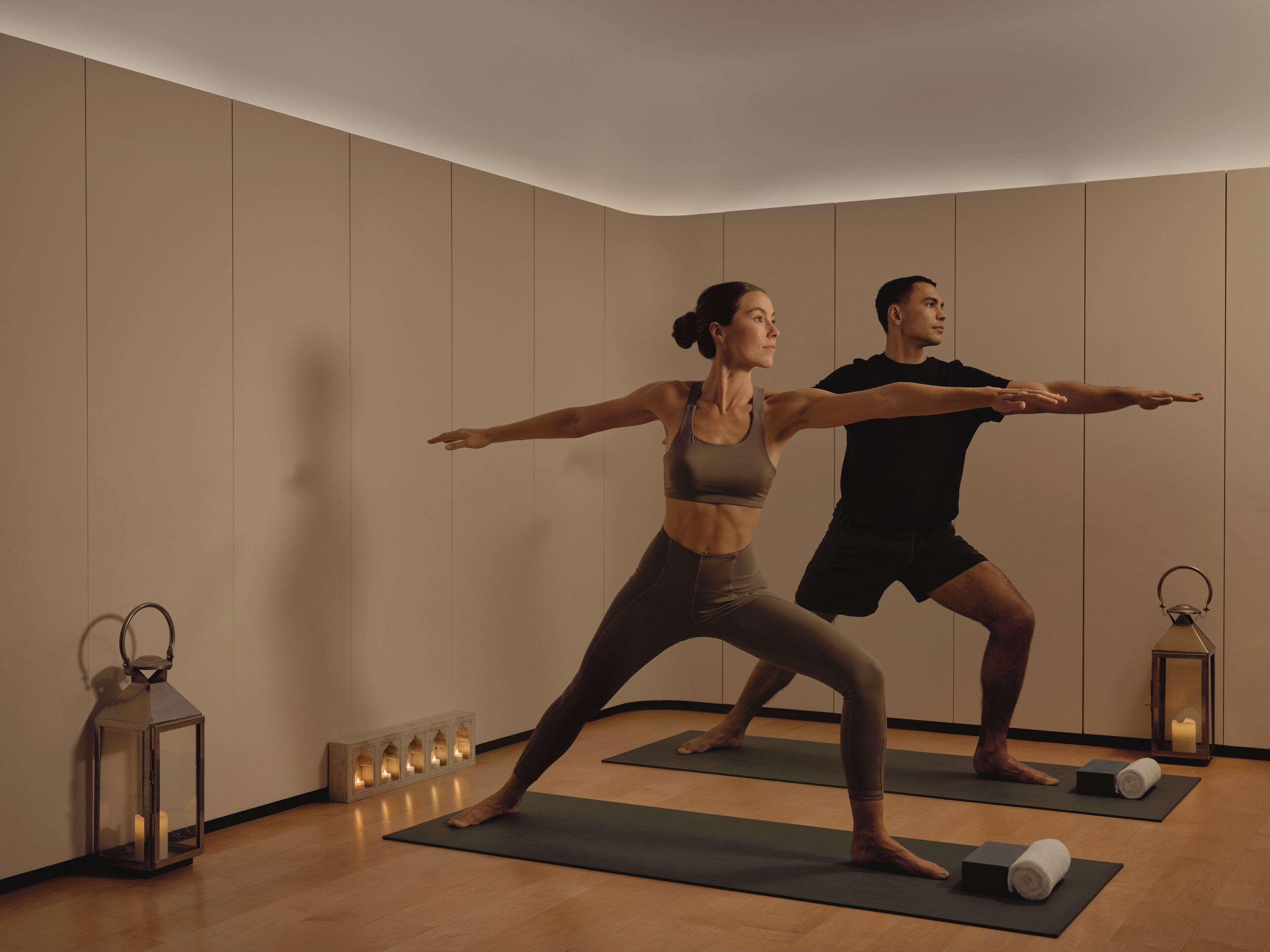 A room with wooden floors, two people on yoga mats, a mirror, and a candle lantern.