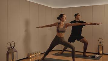 A room with wooden floors, two people on yoga mats, a mirror, and a candle lantern.