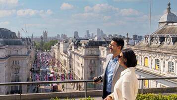 Un couple sur un balcon surplombant une ville, avec des bâtiments historiques et des drapeaux visibles.