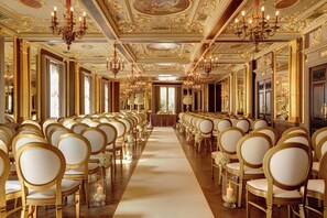 A grand hall with rows of golden chairs and a central aisle, ornate chandeliers, and a marble floor. - Hotel Cafe Royal, London (London)