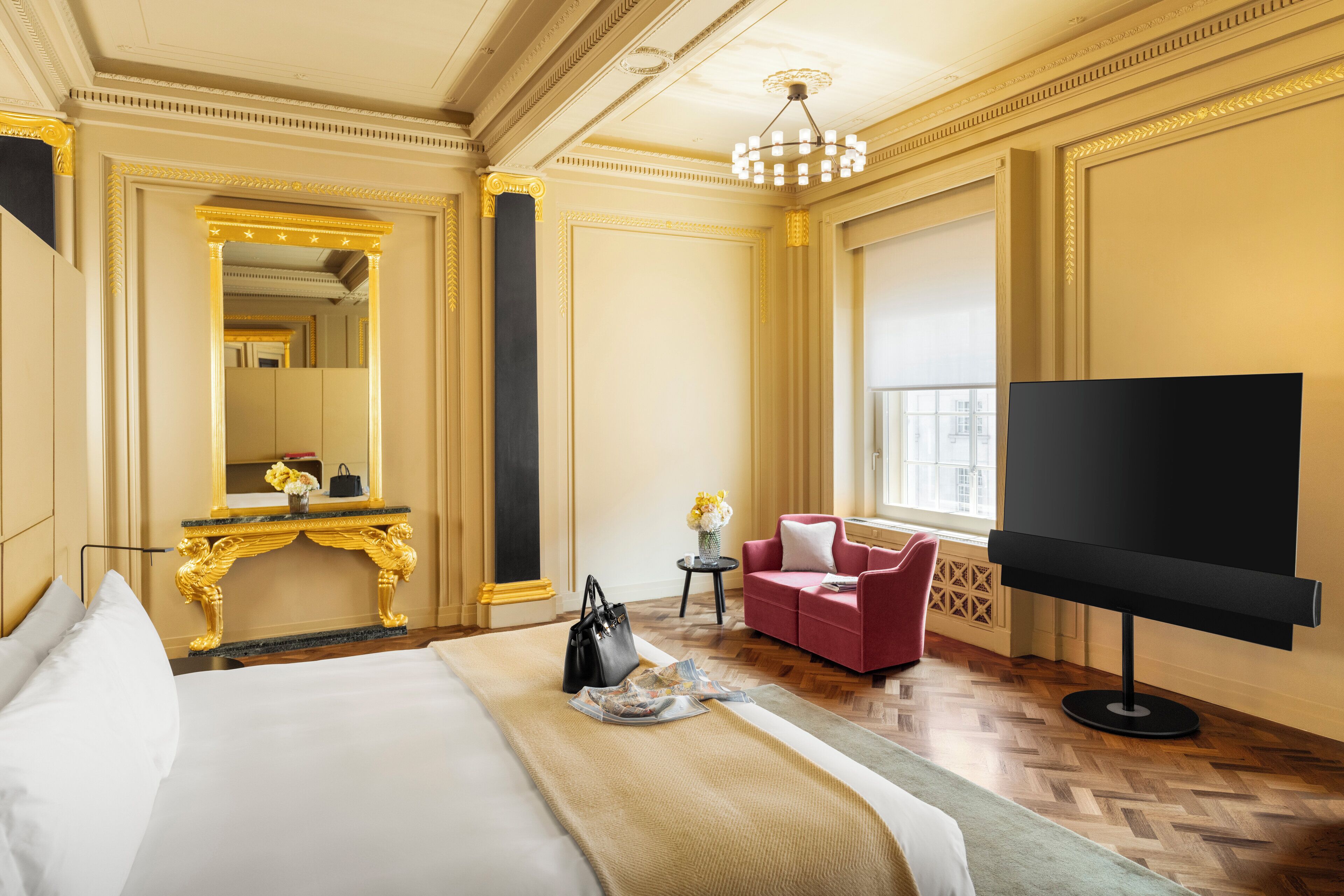 A luxurious hotel room with a large bed, a TV, a red sofa, and a gold-framed mirror.