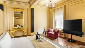 A luxurious hotel room with a large bed, a TV, a red sofa, and a gold-framed mirror.