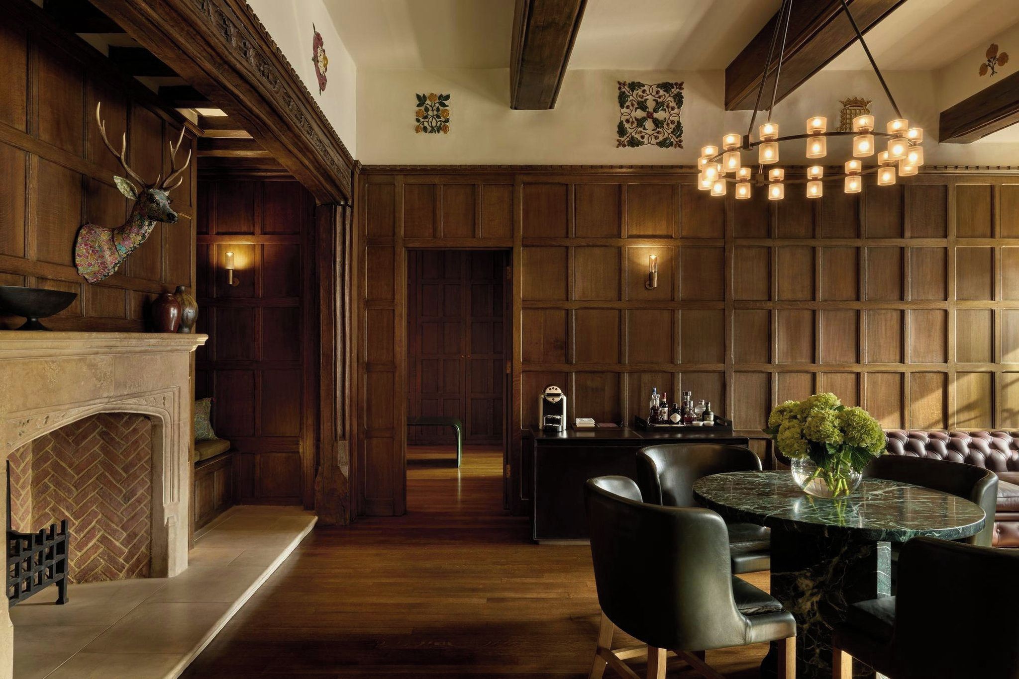 A room with a fireplace, wooden panel walls, a dining area with a round table and chairs, and a bar area with a light fixture.