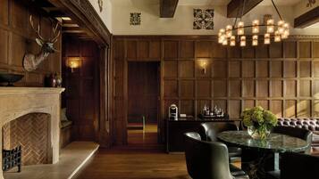 A room with a fireplace, wooden panel walls, a dining area with a round table and chairs, and a bar area with a light fixture.