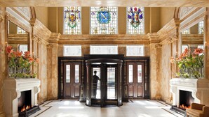 A grand lobby with a revolving door, marble floors, and two fireplaces with floral arrangements. - Hotel Cafe Royal, London (London)