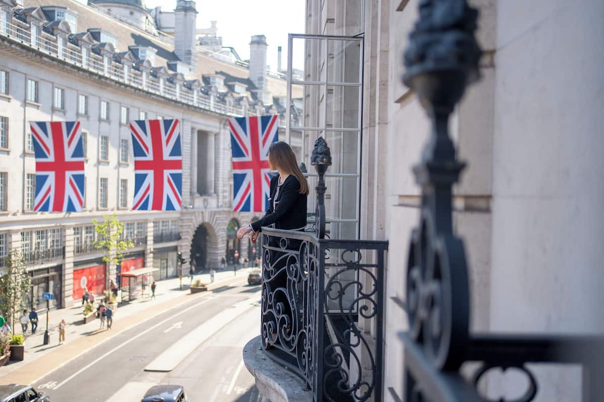 A balcony with ornate metal railings overlooking a street with British flags.