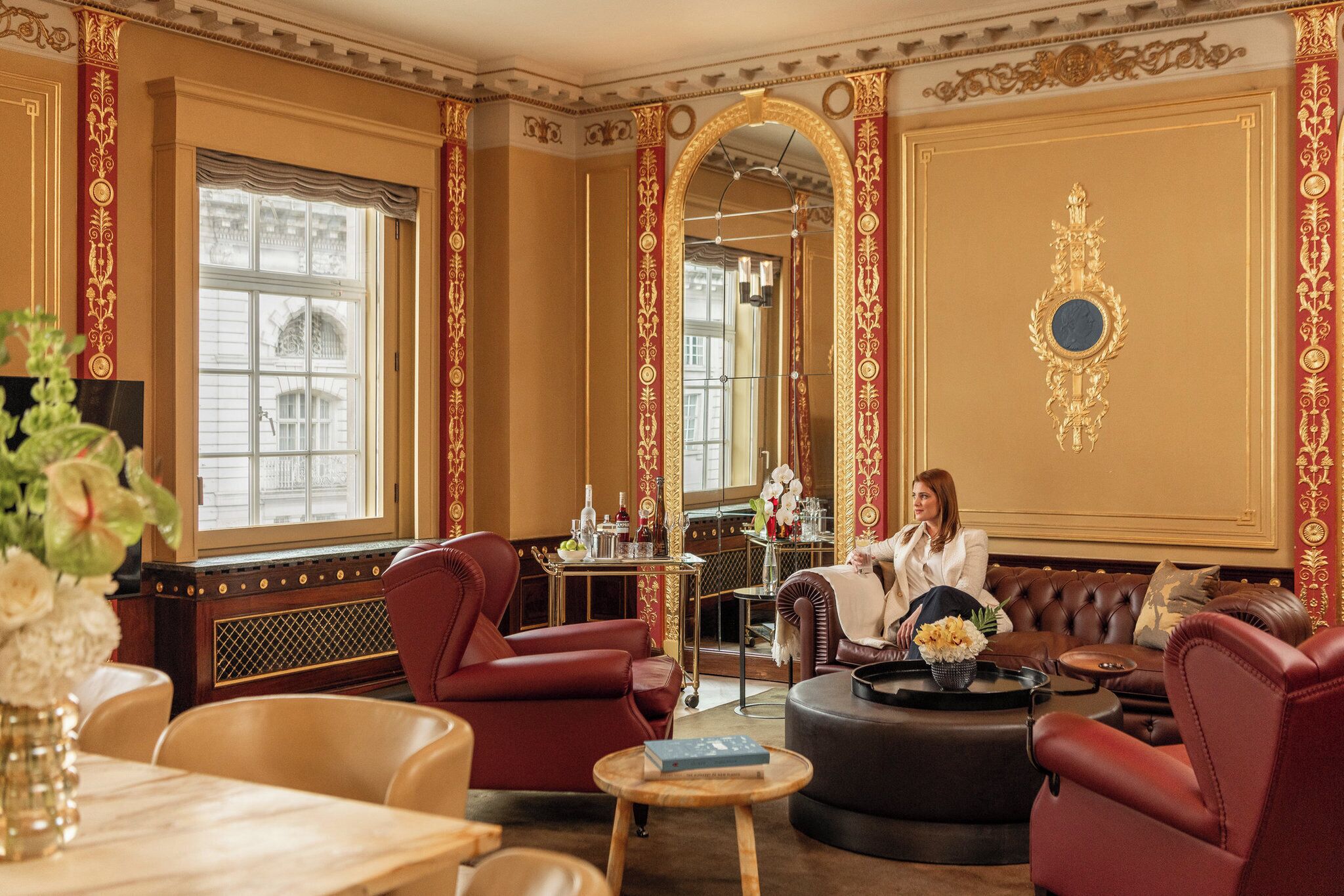 A luxurious room with a large mirror, red upholstered chairs, a leather sofa, and a dining area with a table and chairs.