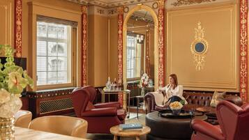 A luxurious room with a large mirror, red upholstered chairs, a leather sofa, and a dining area with a table and chairs.