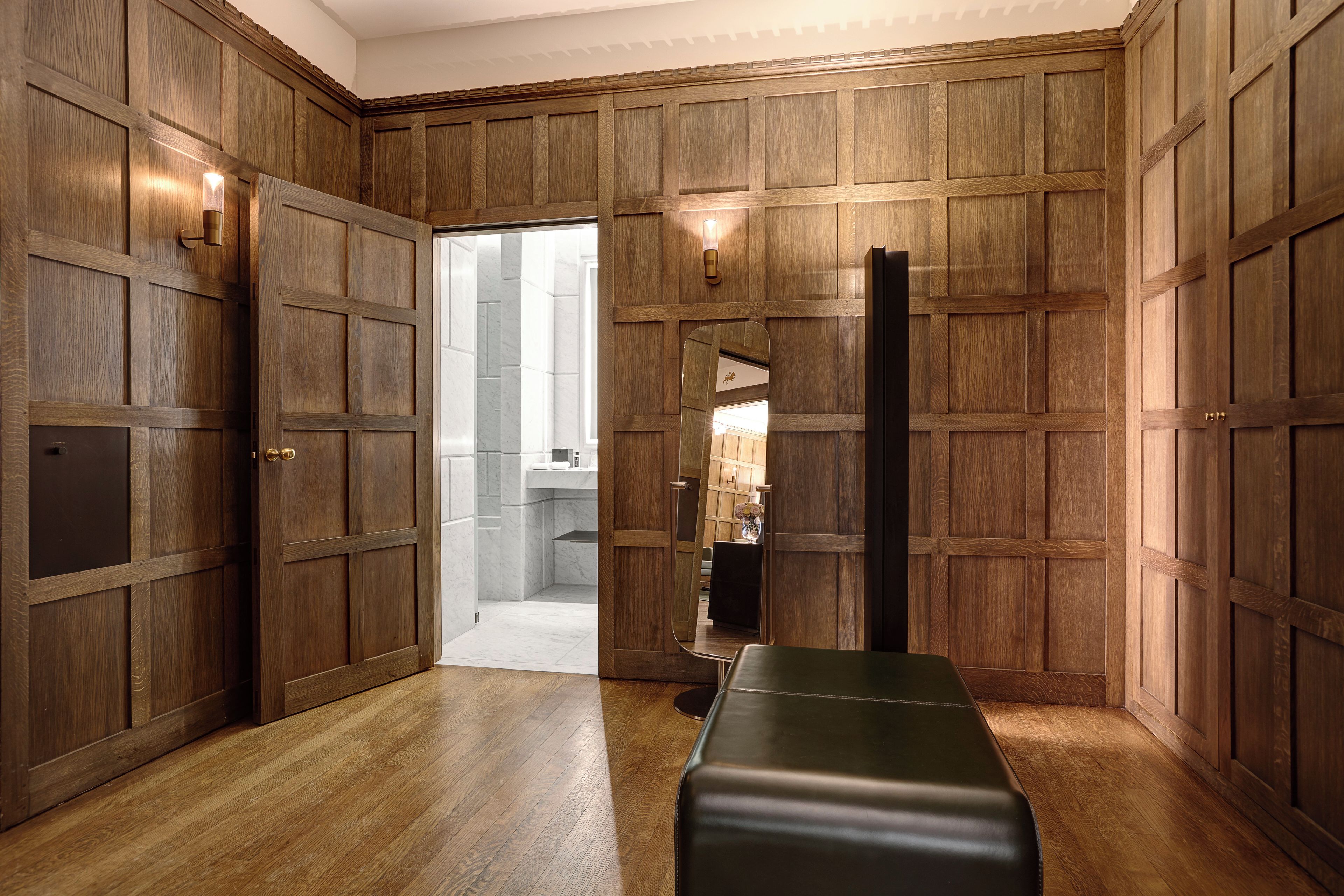 Une pièce avec des lambris en bois, un banc, un miroir et une porte donnant sur une salle de bain.