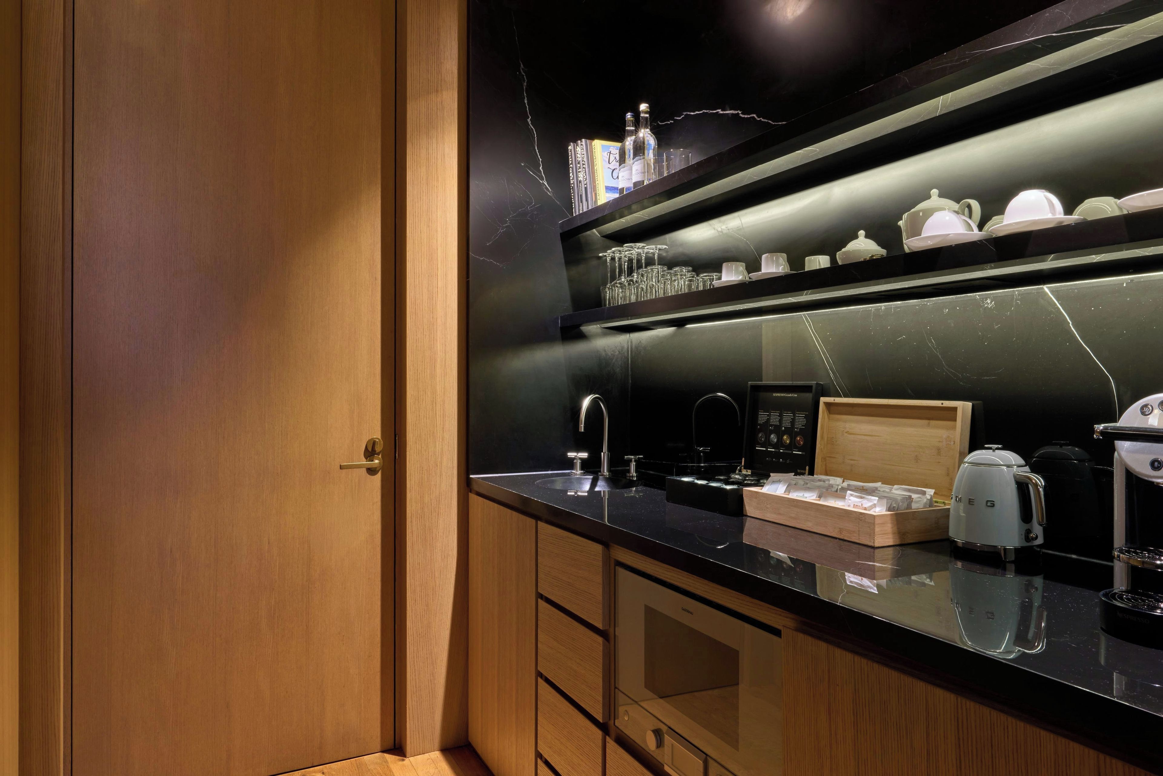Una cocina moderna con cubierta de color negro, una puerta de madera y un estante con cristalería y teteras.