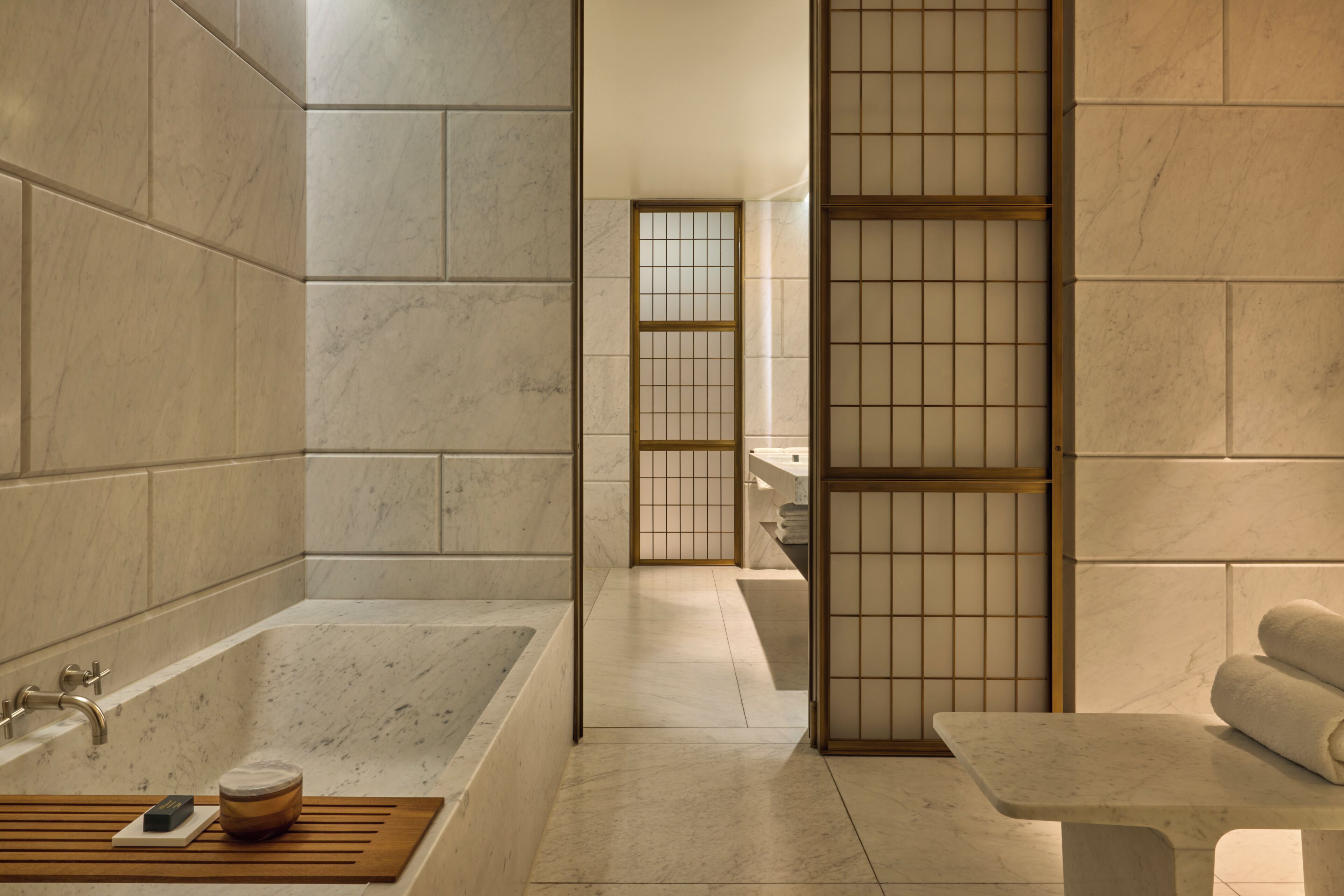 A modern bathroom with a large bathtub, a wooden bench, and a towel rack.