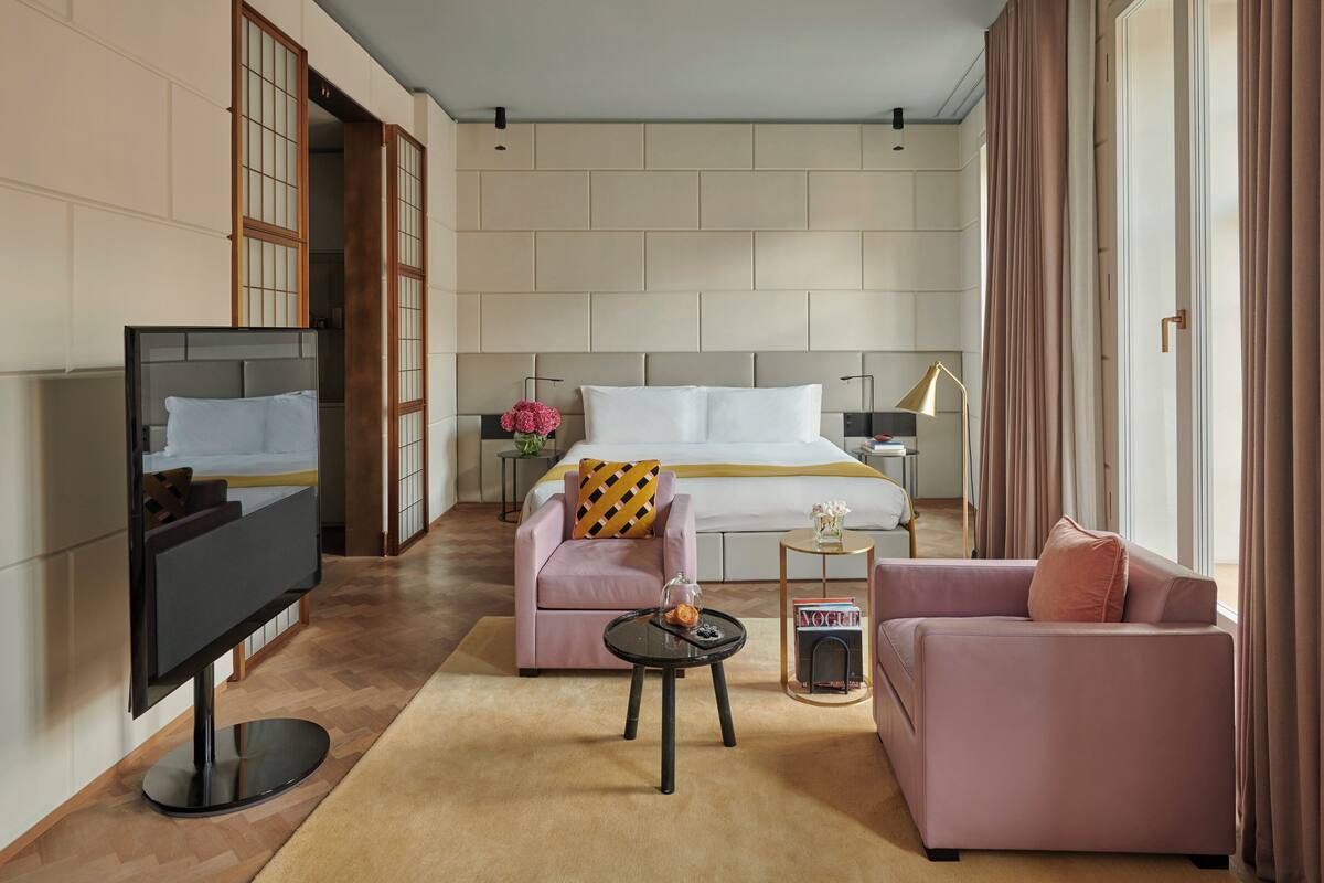A modern hotel room with a large bed, a TV, a sofa, a small table, and a magazine on a side table.