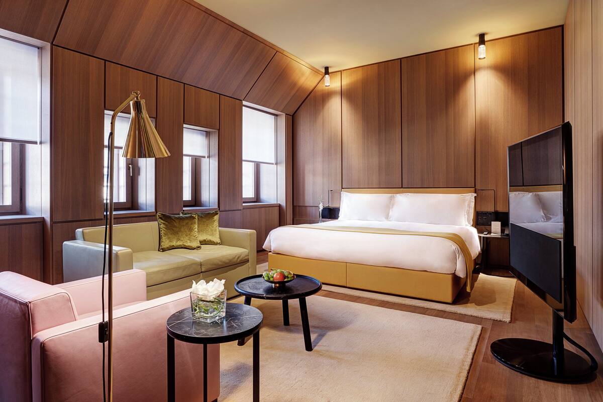 A modern hotel room with a bed, sofa, TV, and a small table with a vase.