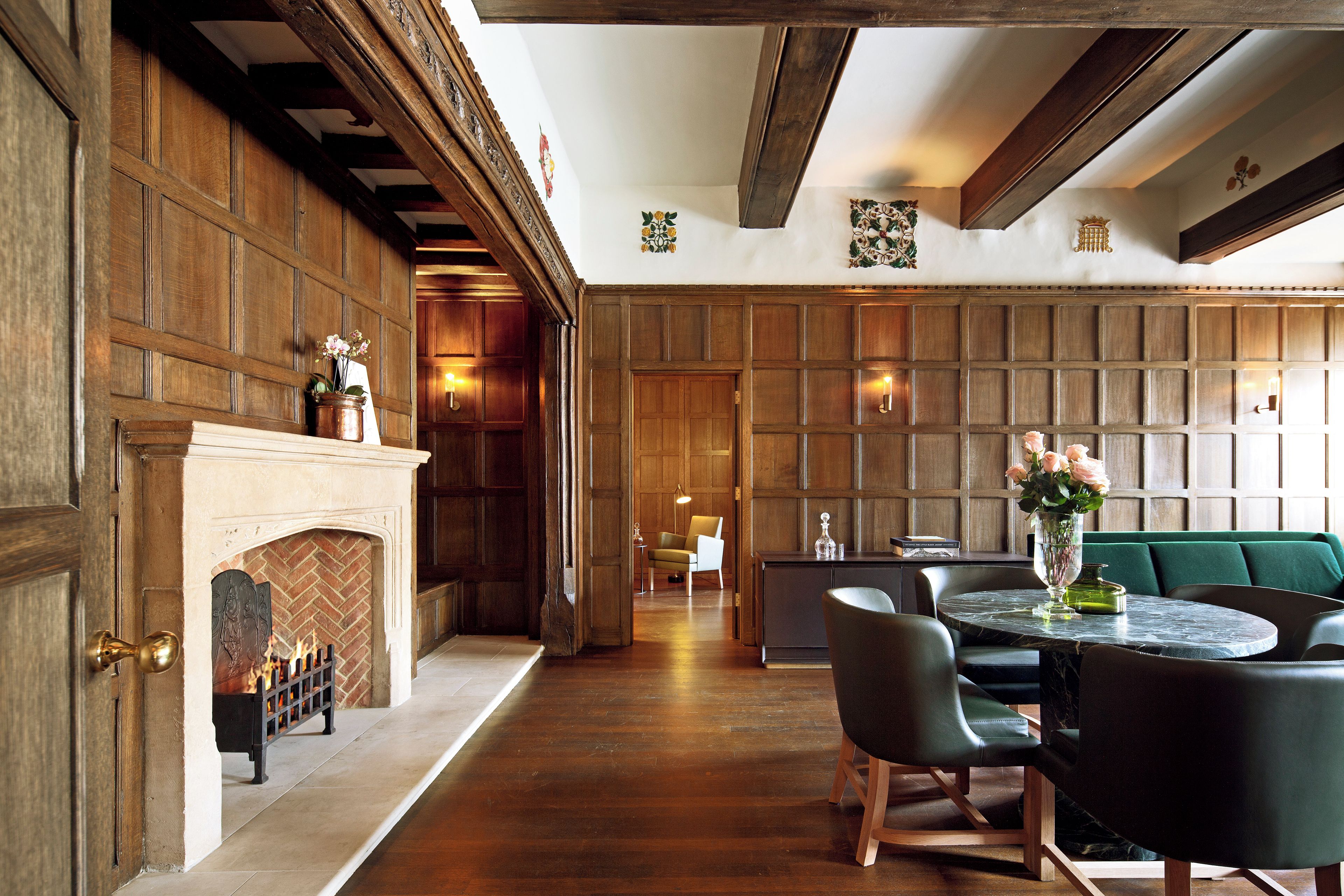 A room with a fireplace, wooden paneling, a dining table with chairs, and a green sofa.