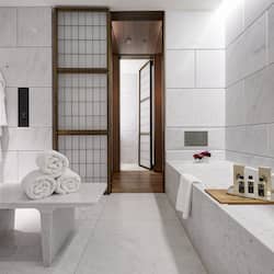 Bathroom features a large bathtub, wooden tray, and a bench with neatly rolled towels.