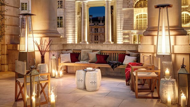 A luxurious seating area with a bench, cushioned chairs, and a table with candles, surrounded by tall columns and ornate architecture. - Hotel Cafe Royal, London (London)