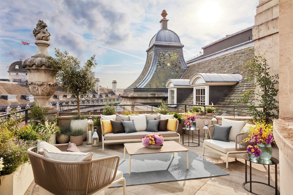 A rooftop terrace with a sofa, chairs, a table, and potted plants.