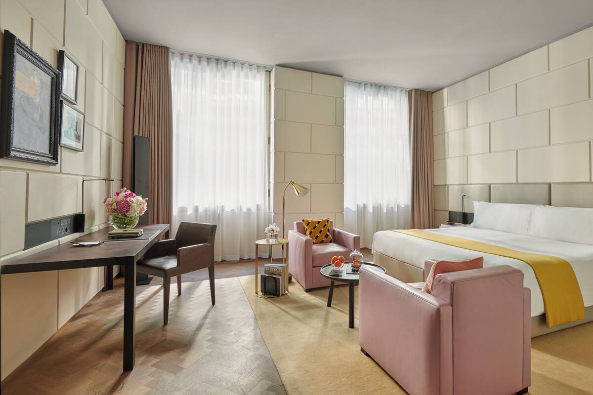 A hotel room with a bed, a desk, a chair, a sofa, and a small table with a lamp.