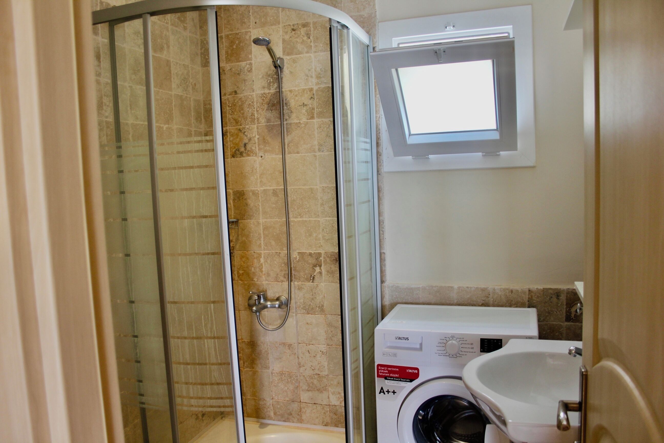 A bathroom with a glass-enclosed shower, a washing machine, and a sink.