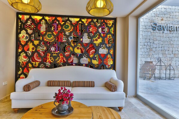 Un sofá blanco con almohadones a rayas, una mesa de centro de madera con un jarrón de flores y una pared colorida con diseños geométricos.