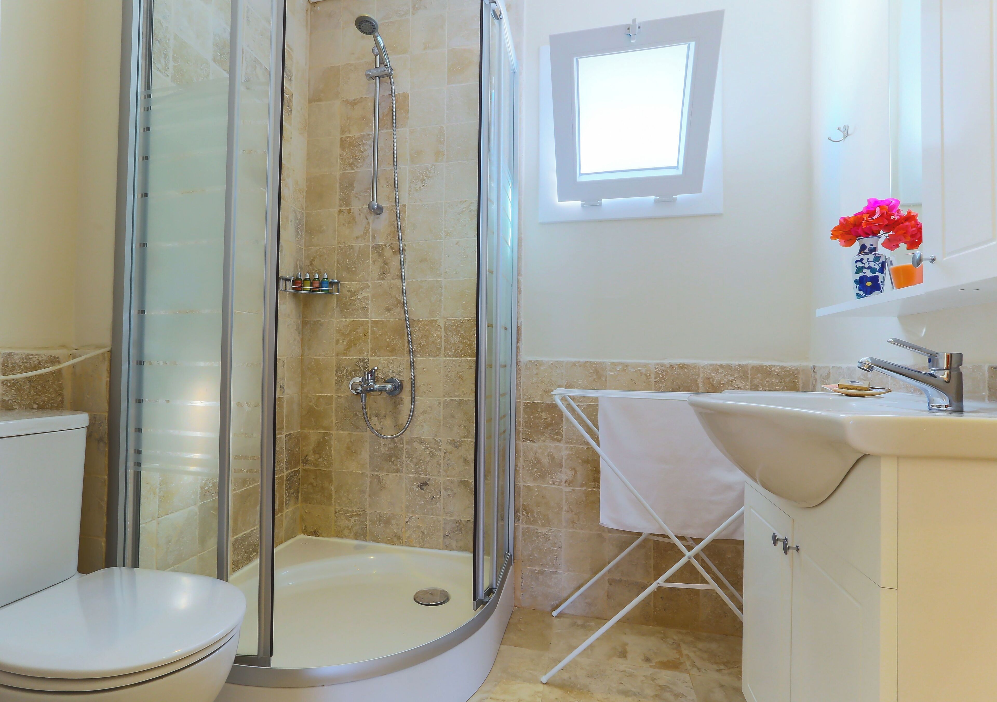 Un baño con ducha de vidrio, inodoro, lavamanos y una ventana pequeña.
