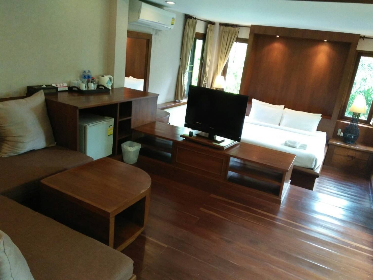 Une chambre d’hôtel avec un plancher en bois, une télévision, un canapé, une petite table, un bureau et une fenêtre avec des rideaux.