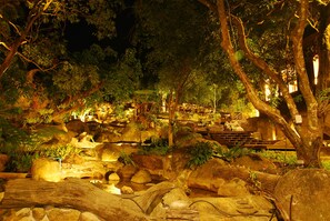 A nighttime outdoor area with illuminated rocks, trees, and a bench.