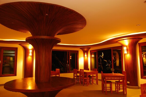A dining area with a central round table surrounded by chairs, wooden columns, and warm ambient lighting. - Bura Resort, Chiang Rai (Chiang Rai)
