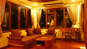 A cozy living room with a sectional sofa, a wooden coffee table, and a dining area with a chair and table. - Bura Resort, Chiang Rai (Chiang Rai)