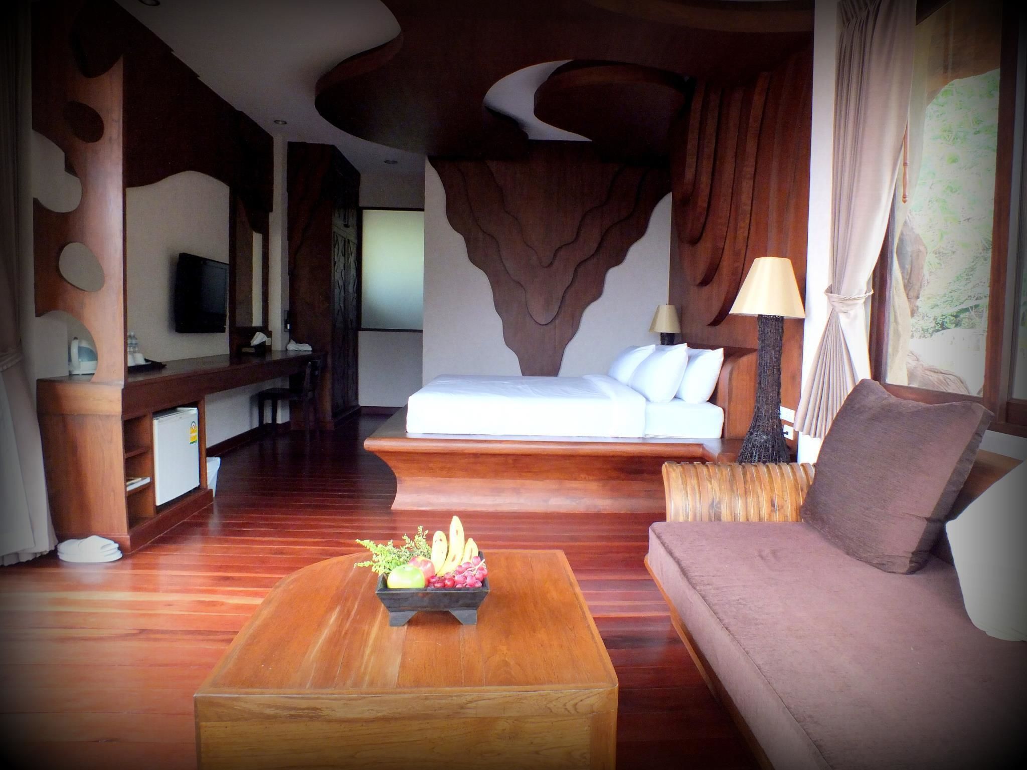 Una habitación de hotel con una cama, un sofá, una mesa de centro con fruta, un televisor y un escritorio.