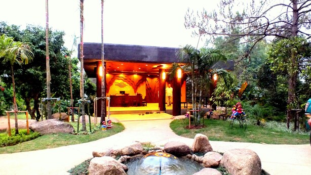 A building with a reception area, a small pond with rocks, and surrounding greenery.