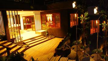 Una casa moderna con terraza de madera, zona de estar interior y vistas al jardín circundante.