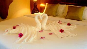 A neatly made bed with two white towels arranged in the shape of swans, adorned with red and pink flowers.