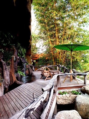 A wooden deck with a rustic design, surrounded by bamboo trees and a small waterfall.