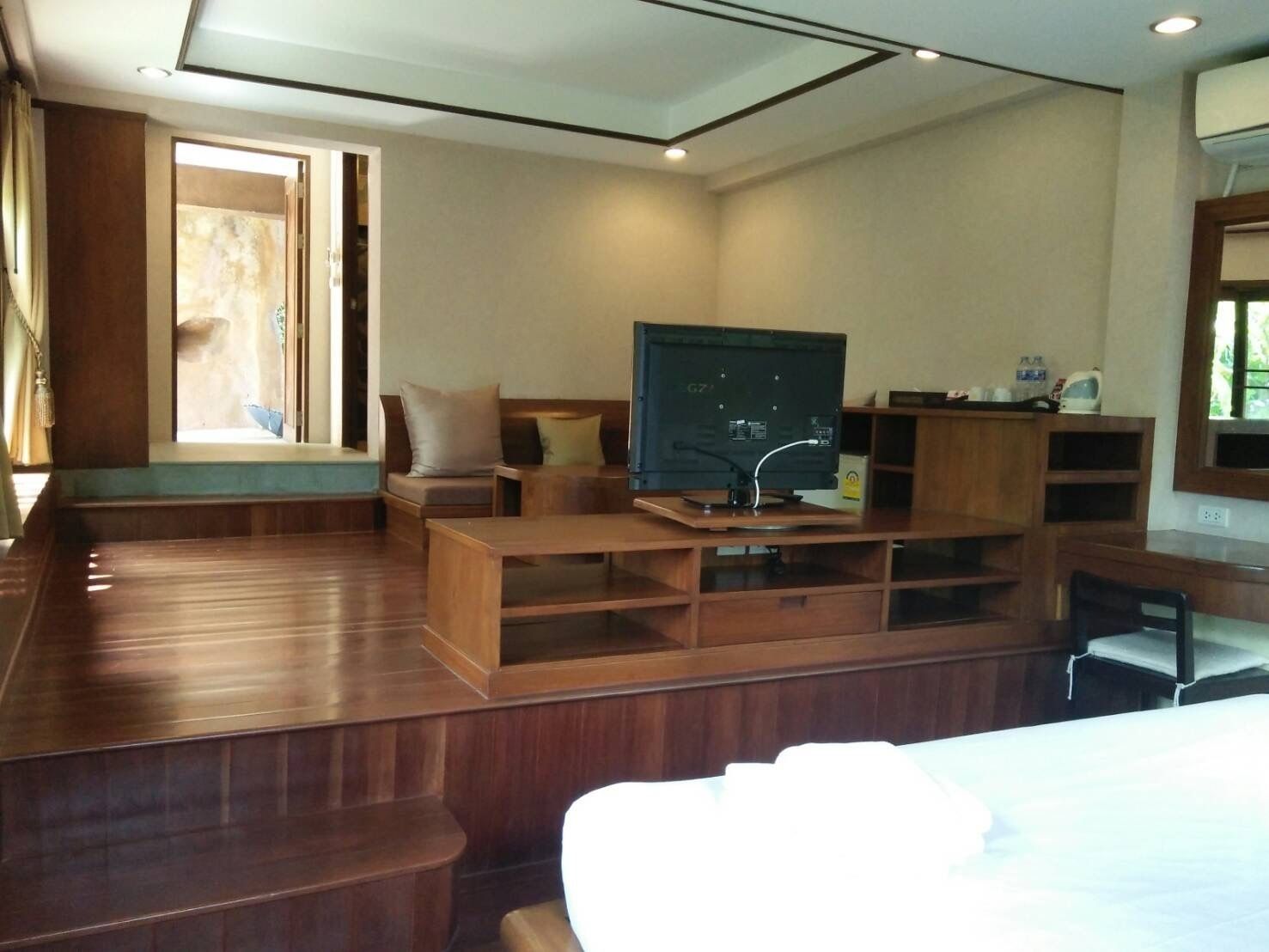 A spacious room with a wooden floor, a large flat-screen TV on a wooden stand, a sofa, and a bed.