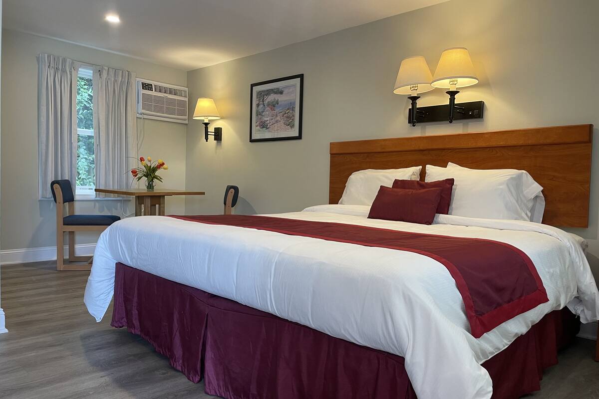 A neatly made bed with white and red bedding, a wooden headboard, and two wall-mounted lamps.