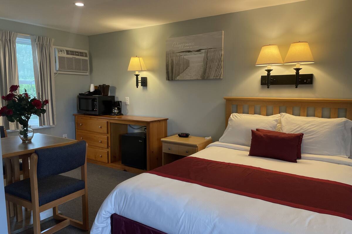 A hotel room with a bed, desk, chair, and a small kitchenette.