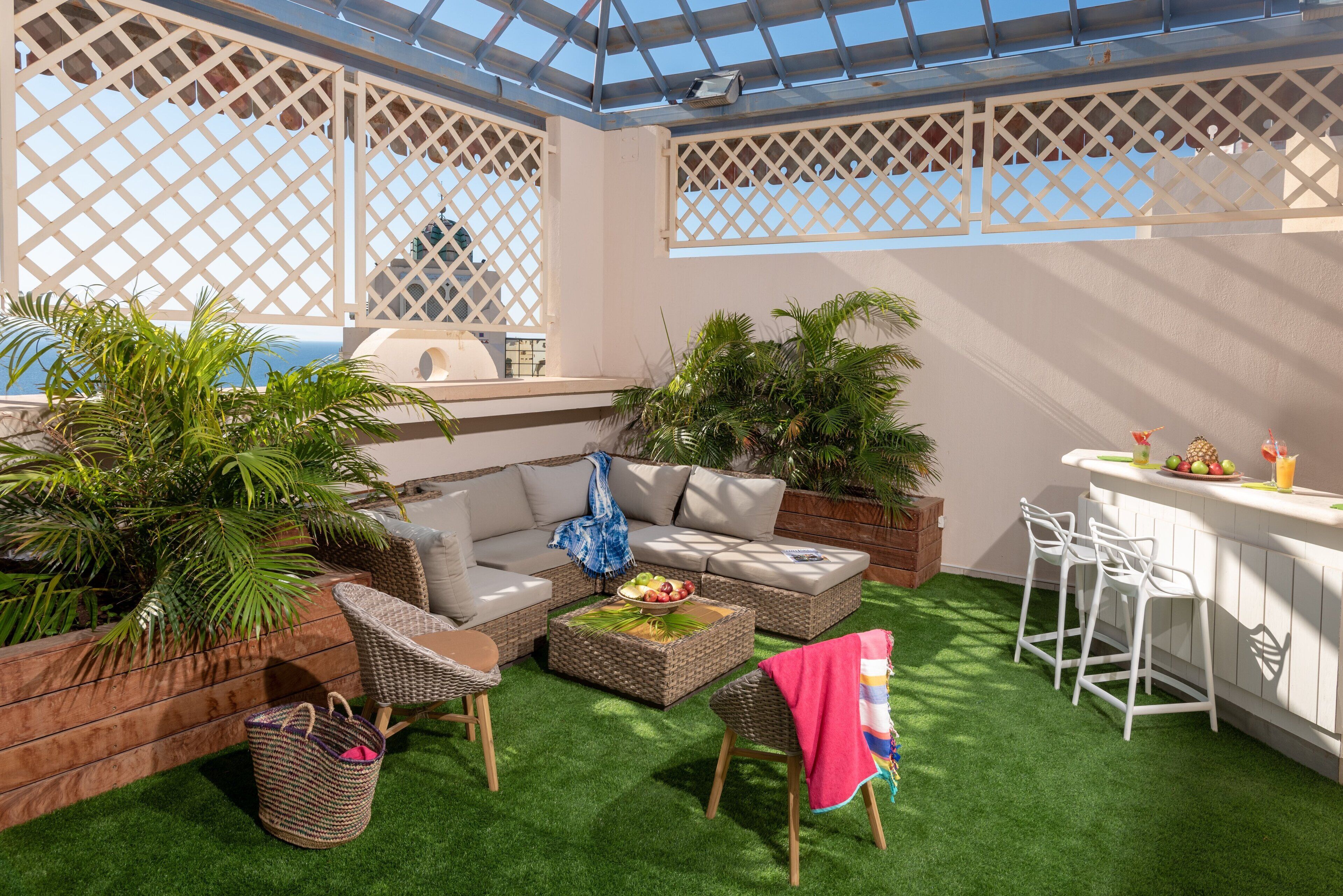 An outdoor patio with a sofa, wicker chairs, a bar area, and potted plants.