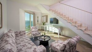 Uma sala de estar moderna com sofá, poltronas, mesa de centro, televisão, escada e vista para o exterior.