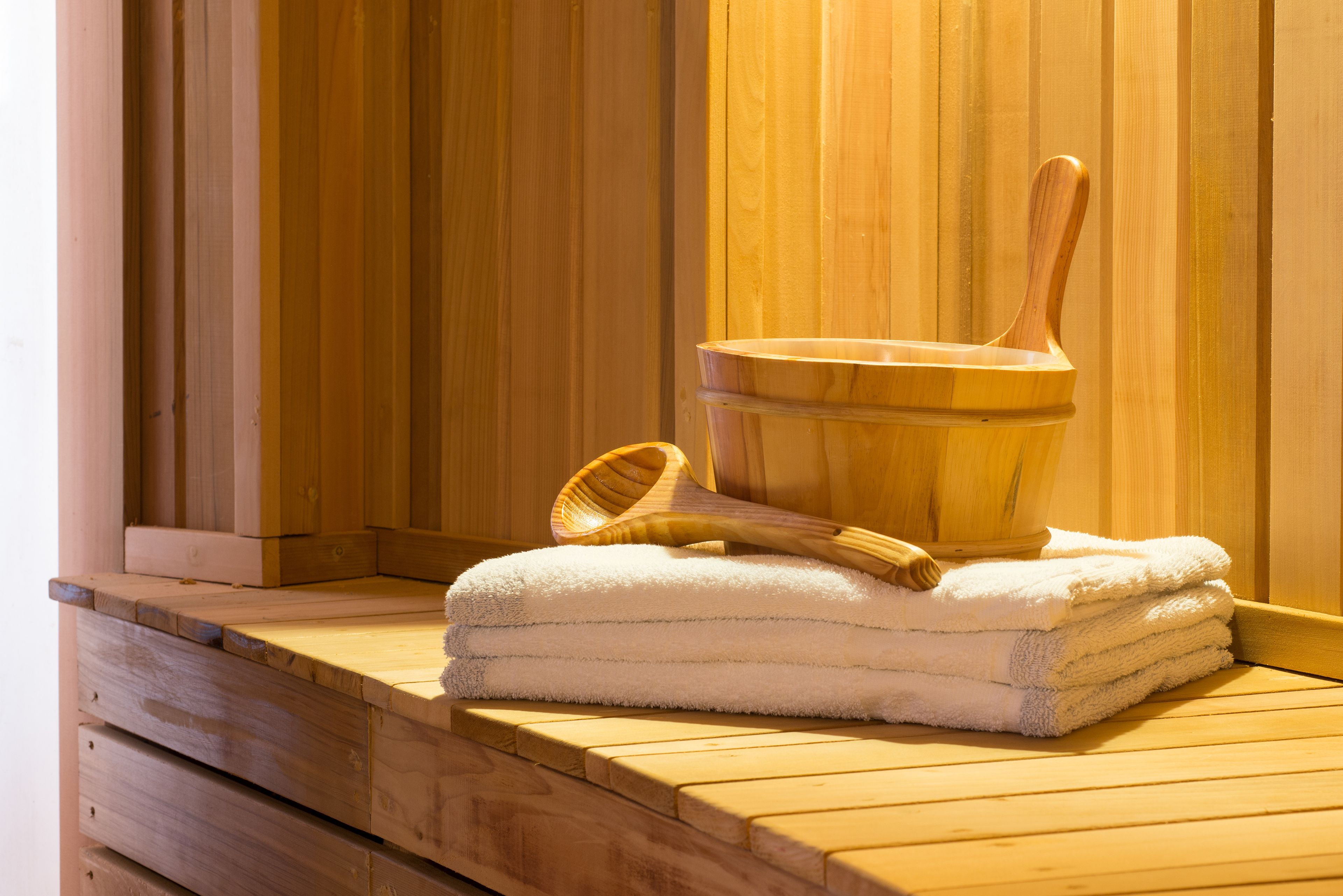 Una sauna de madera con un balde y una cuchara de madera. Toallas blancas apiladas sobre un banco de madera.