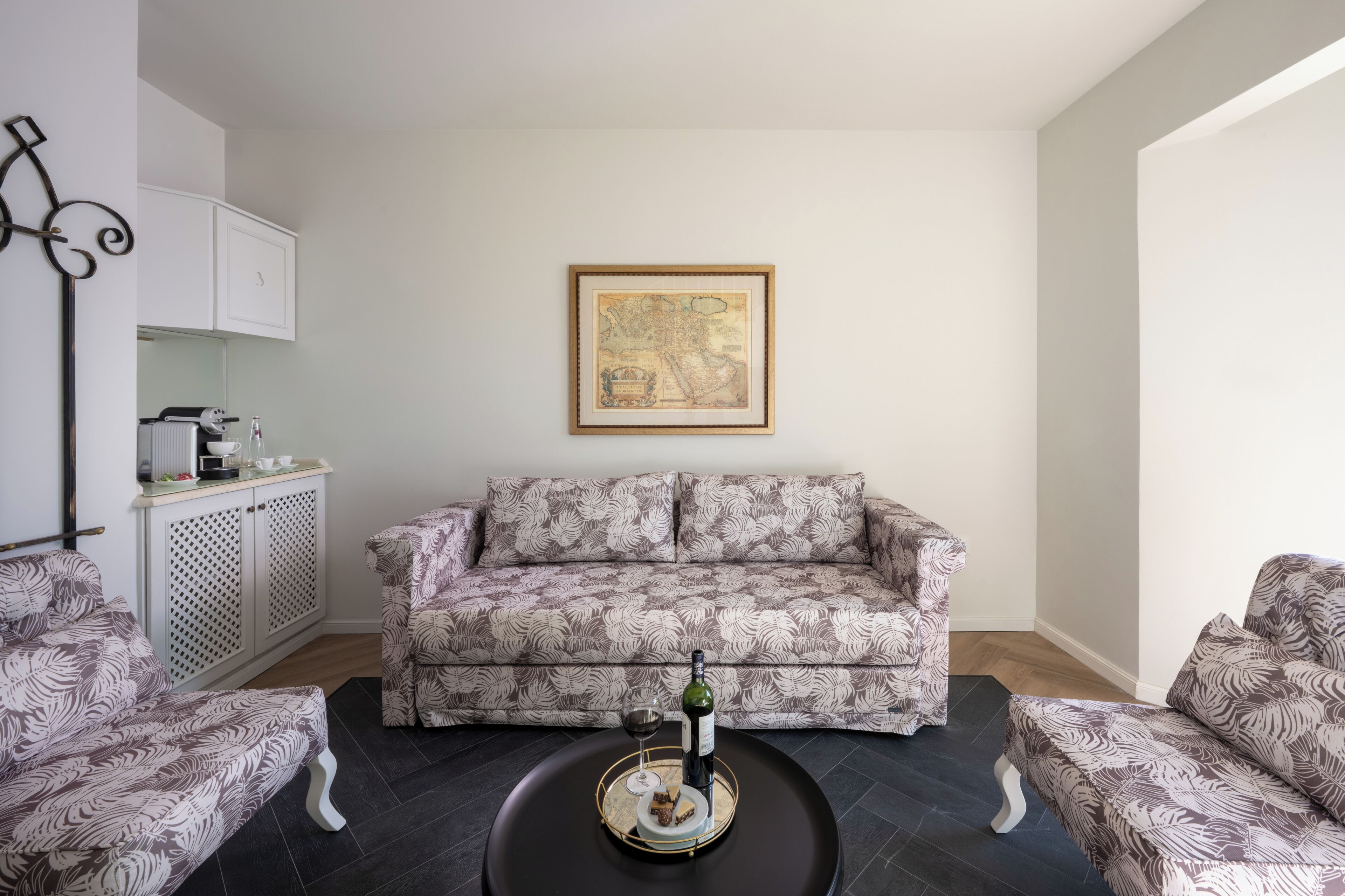 Un salon avec un canapé à motifs, une table basse sur laquelle se trouvent une bouteille et un verre, et une œuvre d’art encadrée accrochée au mur.