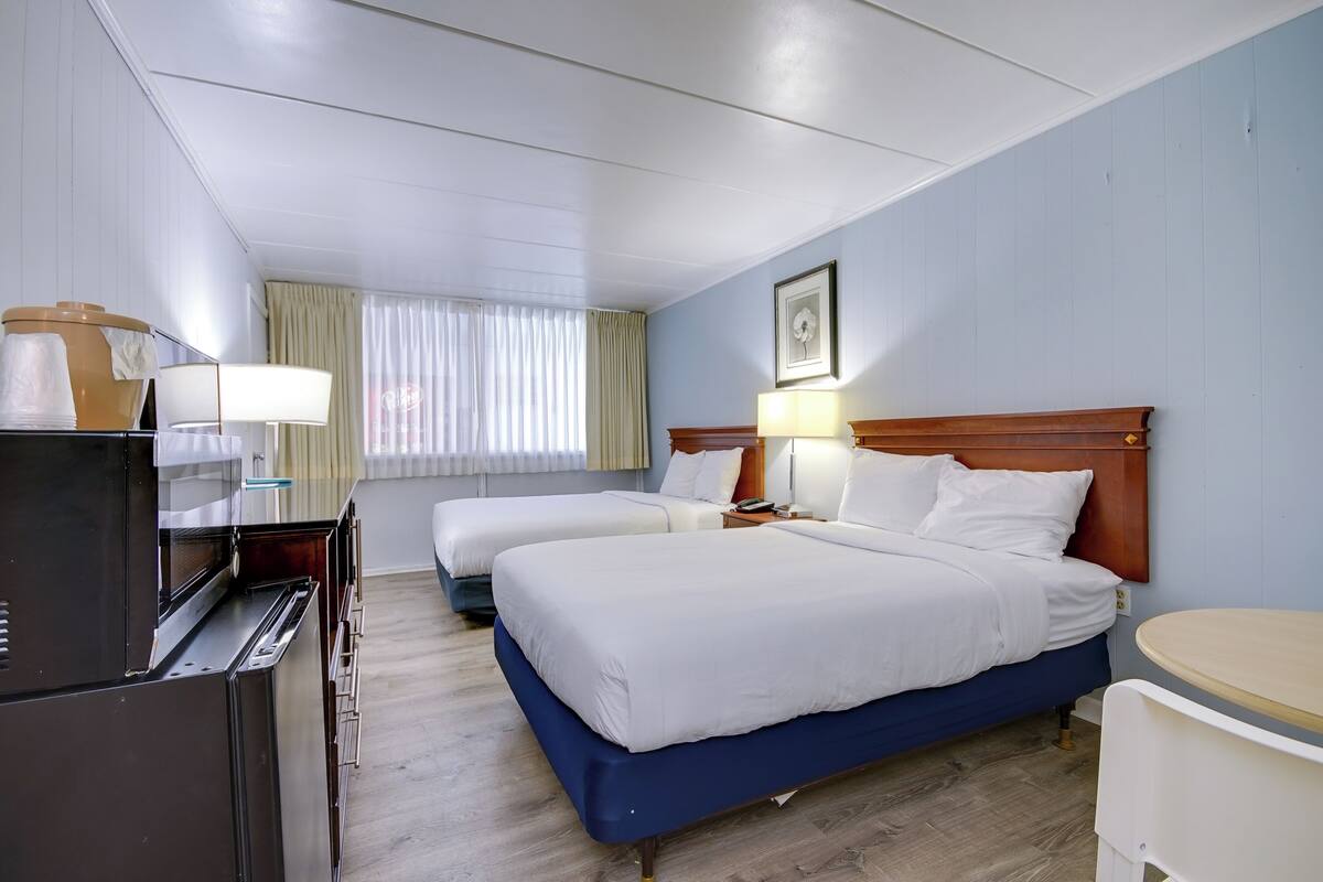 Une chambre d’hôtel avec deux lits, un bureau, une lampe et une fenêtre avec des rideaux.