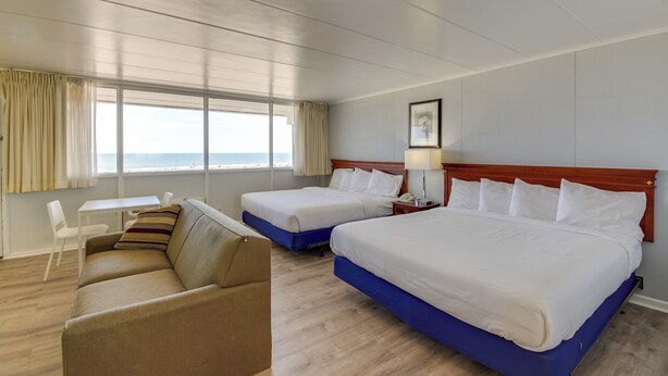 A hotel room with two beds, a sofa, a desk, and a view of the ocean.